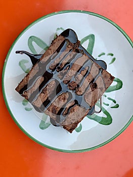 Brownie with Chocolate Sauce Served at Cafe Shop on Orange Surface.