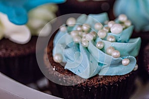 Brownie cupcake muffin with blue whipped cream twirl and white pearl beads topping