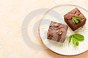 Brownie sweet chocolate dessert with walnuts and meant leaves on craft plate with copy space on pastel beige background.