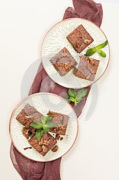 Brownie sweet chocolate dessert with walnuts and meant leaves on craft plate with copy space on pastel beige background.