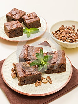 Brownie sweet chocolate dessert with walnuts and meant leaves on craft plate with copy space on pastel beige background.