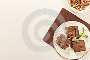 Brownie sweet chocolate dessert with walnuts and meant leaves on craft plate with copy space on pastel beige background.