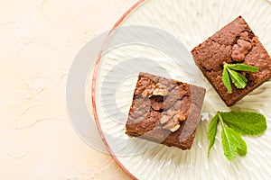 Brownie sweet chocolate dessert with walnuts and meant leaves on craft plate with copy space on pastel beige background.