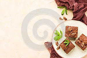 Brownie sweet chocolate dessert with walnuts and meant leaves on craft plate with copy space on pastel beige background.