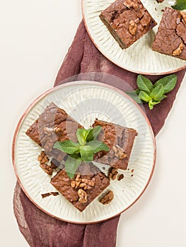 Brownie sweet chocolate dessert with walnuts and meant leaves on craft plate with copy space on pastel beige background.