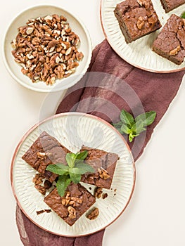 Brownie sweet chocolate dessert with walnuts and meant leaves on craft plate with copy space on pastel beige background.