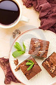 Brownie sweet chocolate dessert with walnuts and meant leaves on craft plate and cup of black coffee.