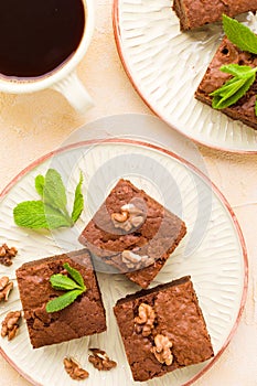 Brownie sweet chocolate dessert with walnuts and meant leaves on craft plate and cup of black coffee.