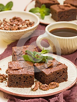 Brownie sweet chocolate dessert with walnuts and meant leaves on craft plate and cup of black coffee.