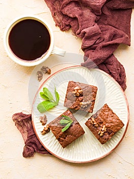 Brownie sweet chocolate dessert with walnuts and meant leaves on craft plate and cup of black coffee.