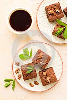 Brownie sweet chocolate dessert with walnuts and meant leaves on craft plate and cup of black coffee.