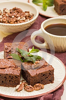 Brownie sweet chocolate dessert with walnuts and meant leaves on craft plate and cup of black coffee.