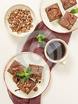 Brownie sweet chocolate dessert with walnuts and meant leaves on craft plate and cup of black coffee.