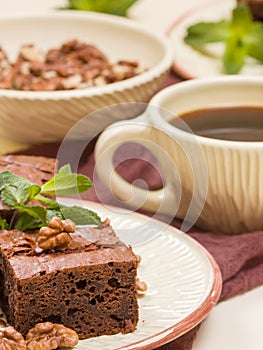 Brownie sweet chocolate dessert with walnuts and meant leaves on craft plate and cup of black coffee.
