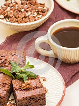 Brownie sweet chocolate dessert with walnuts and meant leaves on craft plate and cup of black coffee.