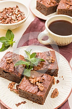 Brownie sweet chocolate dessert with walnuts and meant leaves on craft plate and cup of black coffee.