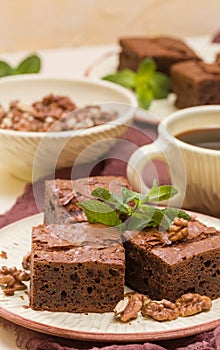 Brownie sweet chocolate dessert with walnuts and meant leaves on craft plate and cup of black coffee.