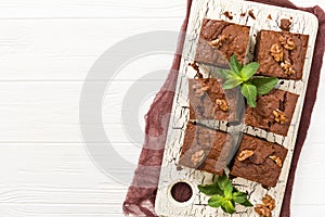 Brownie sweet chocolate dessert with walnuts and meant leaves on retro board with copy space on pastel beige background.