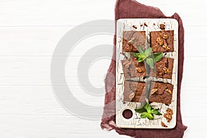 Brownie sweet chocolate dessert with walnuts and meant leaves on retro board with copy space on pastel beige background.