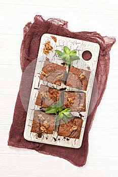 Brownie sweet chocolate dessert with walnuts and meant leaves on retro board with copy space on pastel beige background.