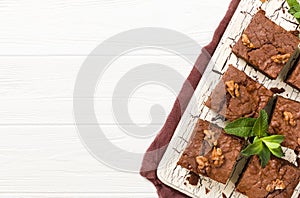 Brownie sweet chocolate dessert with walnuts and meant leaves on retro board with copy space on pastel beige background.