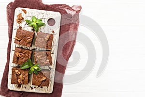 Brownie sweet chocolate dessert with walnuts and meant leaves on retro board with copy space on pastel beige background.