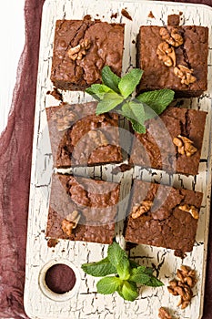 Brownie sweet chocolate dessert with walnuts and meant leaves on retro board with copy space on pastel beige background.