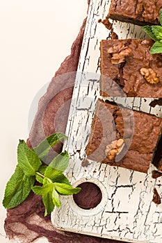 Brownie sweet chocolate dessert with walnuts and meant leaves on retro board with copy space on pastel beige background.