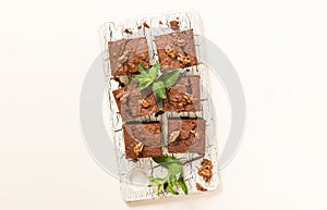 Brownie sweet chocolate dessert with walnuts and meant leaves on retro board with copy space on pastel beige background.