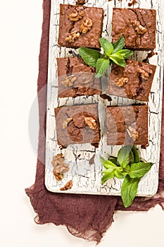 Brownie sweet chocolate dessert with walnuts and meant leaves on retro board with copy space on pastel beige background.