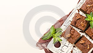 Brownie sweet chocolate dessert with walnuts and meant leaves on retro board with copy space on pastel beige background.