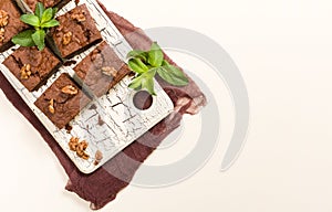 Brownie sweet chocolate dessert with walnuts and meant leaves on retro board with copy space on pastel beige background.