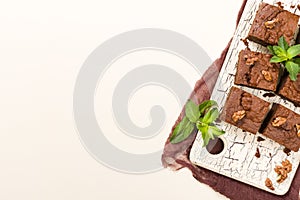 Brownie sweet chocolate dessert with walnuts and meant leaves on retro board with copy space on pastel beige background.