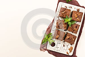 Brownie sweet chocolate dessert with walnuts and meant leaves on retro board with copy space on pastel beige background.