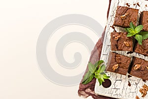 Brownie sweet chocolate dessert with walnuts and meant leaves on retro board with copy space on pastel beige background.