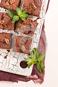 Brownie sweet chocolate dessert with walnuts and meant leaves on retro board with copy space on pastel beige background.