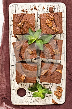 Brownie sweet chocolate dessert with walnuts and meant leaves on retro board with copy space on pastel beige background. photo