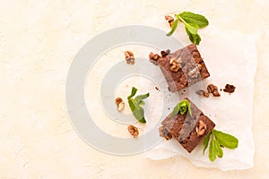 Brownie sweet chocolate dessert with walnuts and meant leaves on white paper with copy space on pastel beige background.