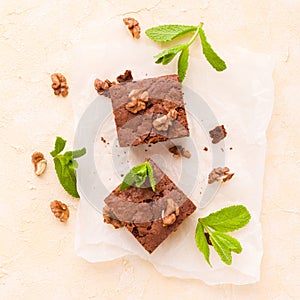 Brownie sweet chocolate dessert with walnuts and meant leaves on white paper with copy space on pastel beige background.