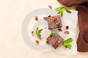 Brownie sweet chocolate dessert with walnuts and meant leaves on white paper with copy space on pastel beige background.