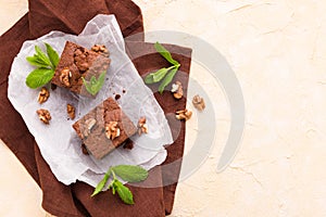 Brownie sweet chocolate dessert with walnuts and meant leaves on white paper with copy space on pastel beige background.