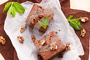 Brownie sweet chocolate dessert with walnuts and meant leaves on white paper with copy space on pastel beige background.