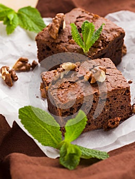 Brownie sweet chocolate dessert with walnuts and meant leaves on white paper with copy space on pastel beige background.