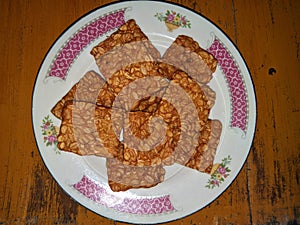 Brownish yellow tempeh on a white plate with floral motifs. On a brown wooden table