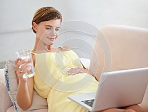 Browsing through the pregnancy blogs. a beautiful pregnant woman enjoying a glass of water while using a laptop at home.