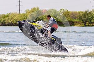 BRP Sea-Doo jet ski driver jumping on water bike and splashing at sunset by river bank at countryside. Man on jet ski in action.