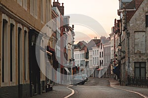 narrow street with beautiful old houses and cars at sunset, brugge, belgium