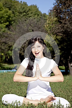 Brunet yoga girl on green grass in park.