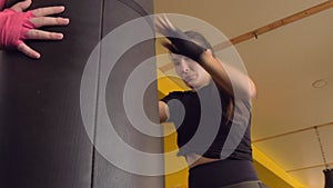 A brunette Asian girl in black boxing bandages beats her knees on a punching bag