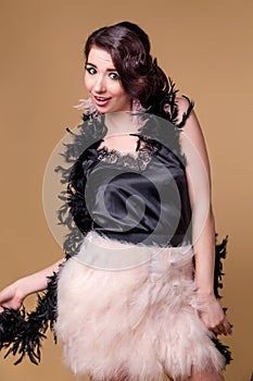 Brunette beautiful woman in boa from ostrich feathers is  fooling around and grimacing on a beige background